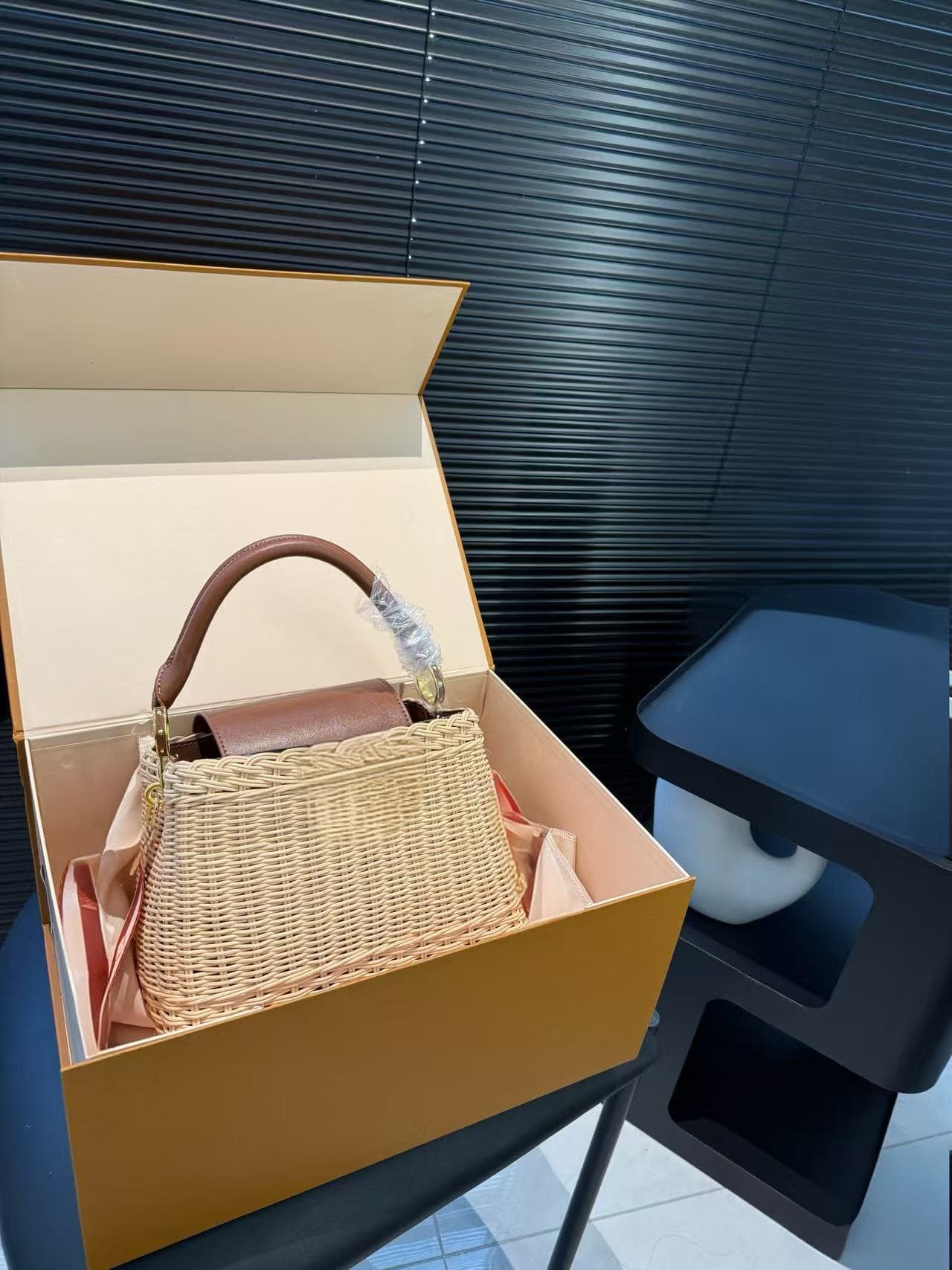 The NoePurse handbag features woven raffia and leather trim, offering multiple carrying options and styling choices.