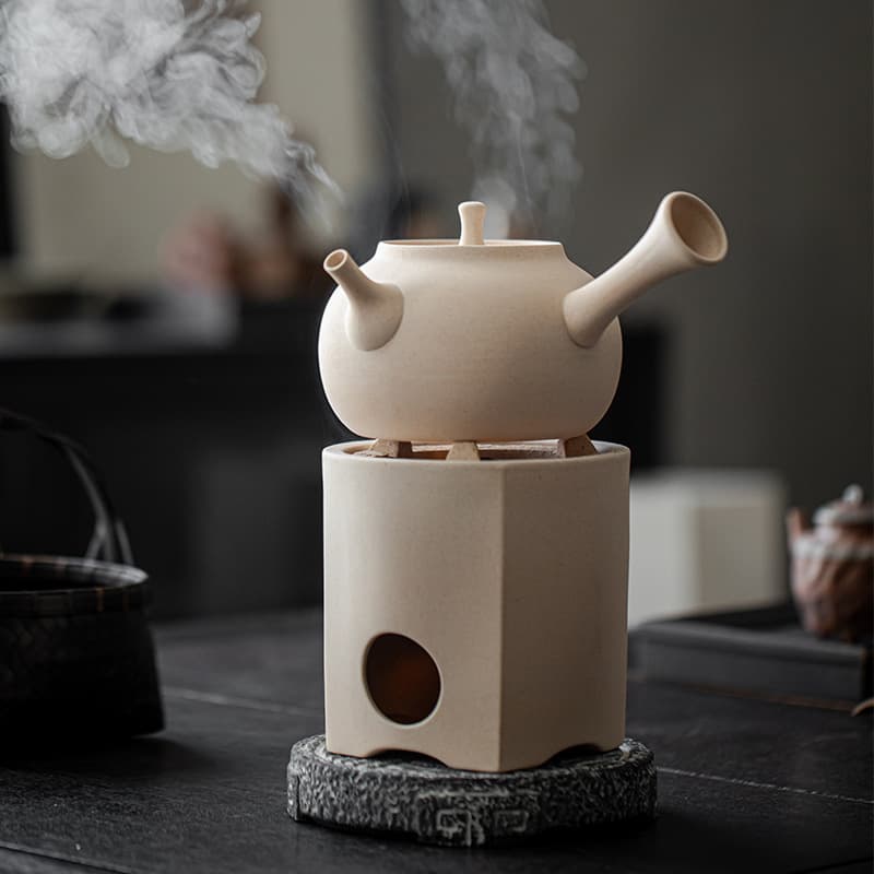 Tea brewing carbon stove set with ceramic side-handle kettle, wind stove, and alcohol burner for boiling water and steeping tea.