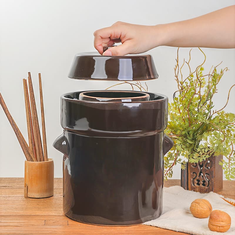 Ceramic pickle jar with stone weight for fermenting and pickling food, includes optional stirring stick for home use.