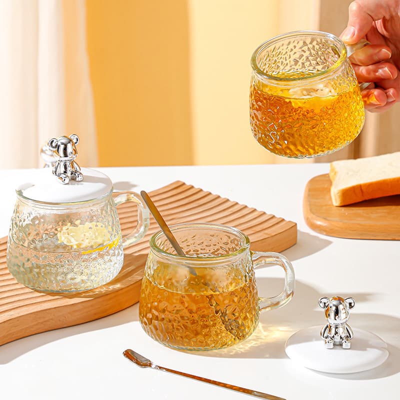 Dropshipping and wholesale of bear-patterned hammered glass mugs, stylish and trendy, with lids, spoons, and handles, perfect for water or coffee.