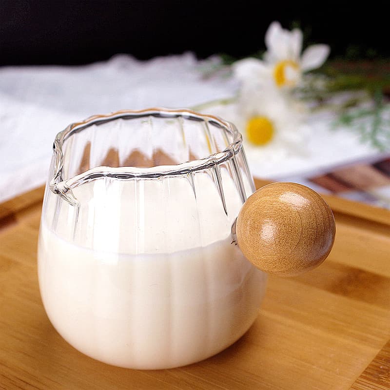 Mini Japanese-style glass milk jug with wooden handle and spout, perfect for making espresso.