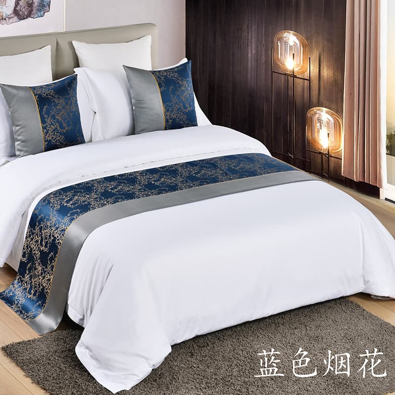 The hotel features a modern, luxurious European-style bed runner and blanket, along with dark blue classic hotel linens, cushions, and throw pillows.