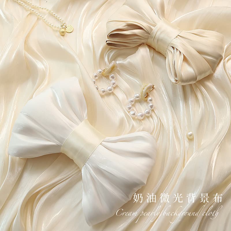 Reflective silk fabric backdrop for high-end jewelry photography; props include bow-shaped pleats.